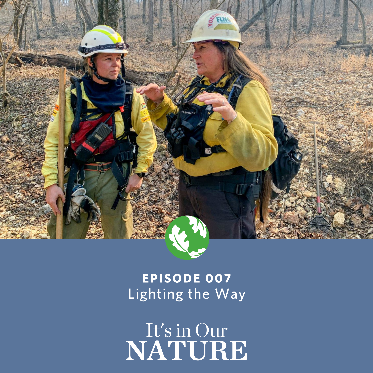 Two women wearing yellow fire gear talking in a forested area. 