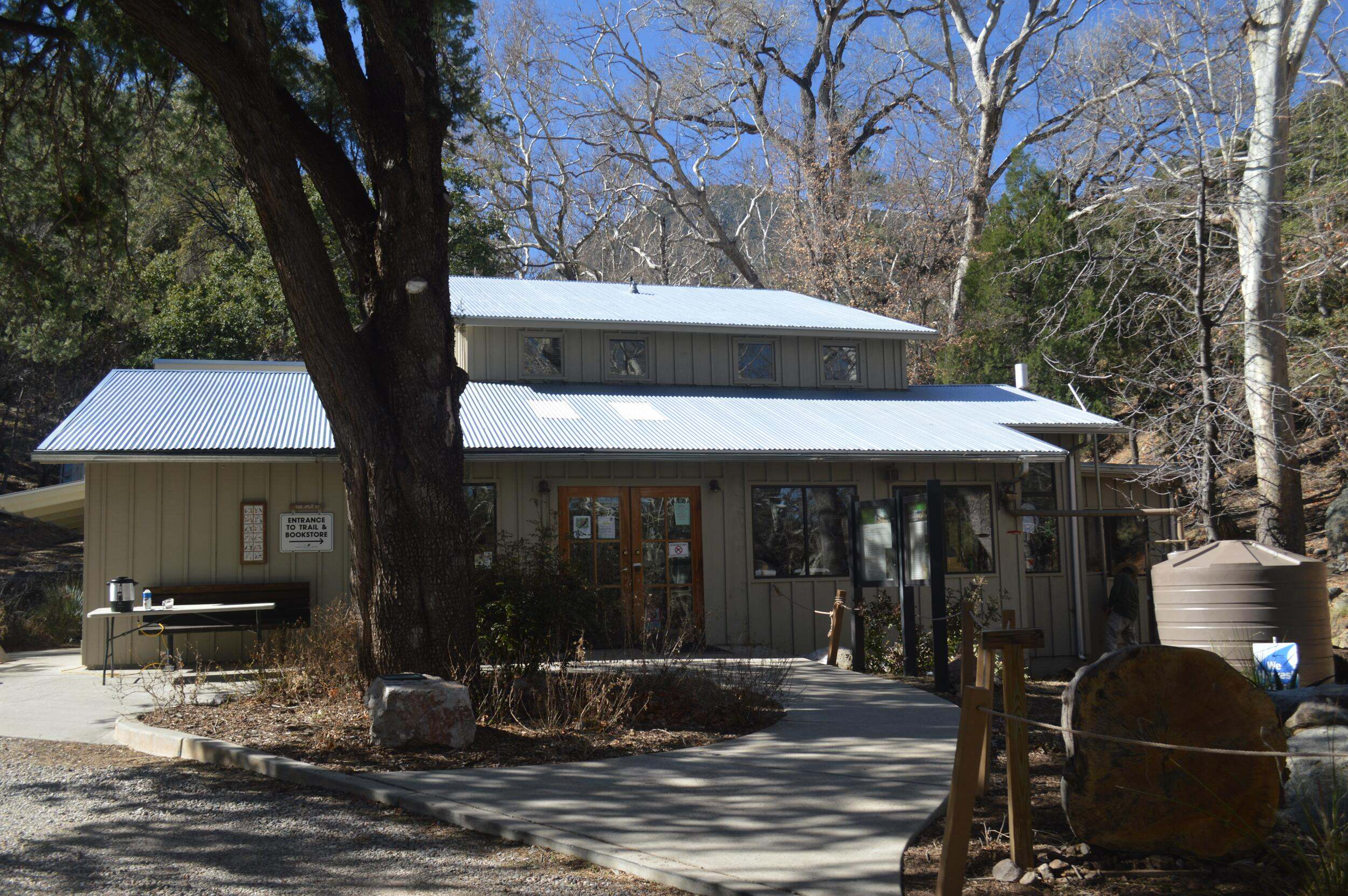 View of the visitor center building with a large tree in front and smaller trees behind it.