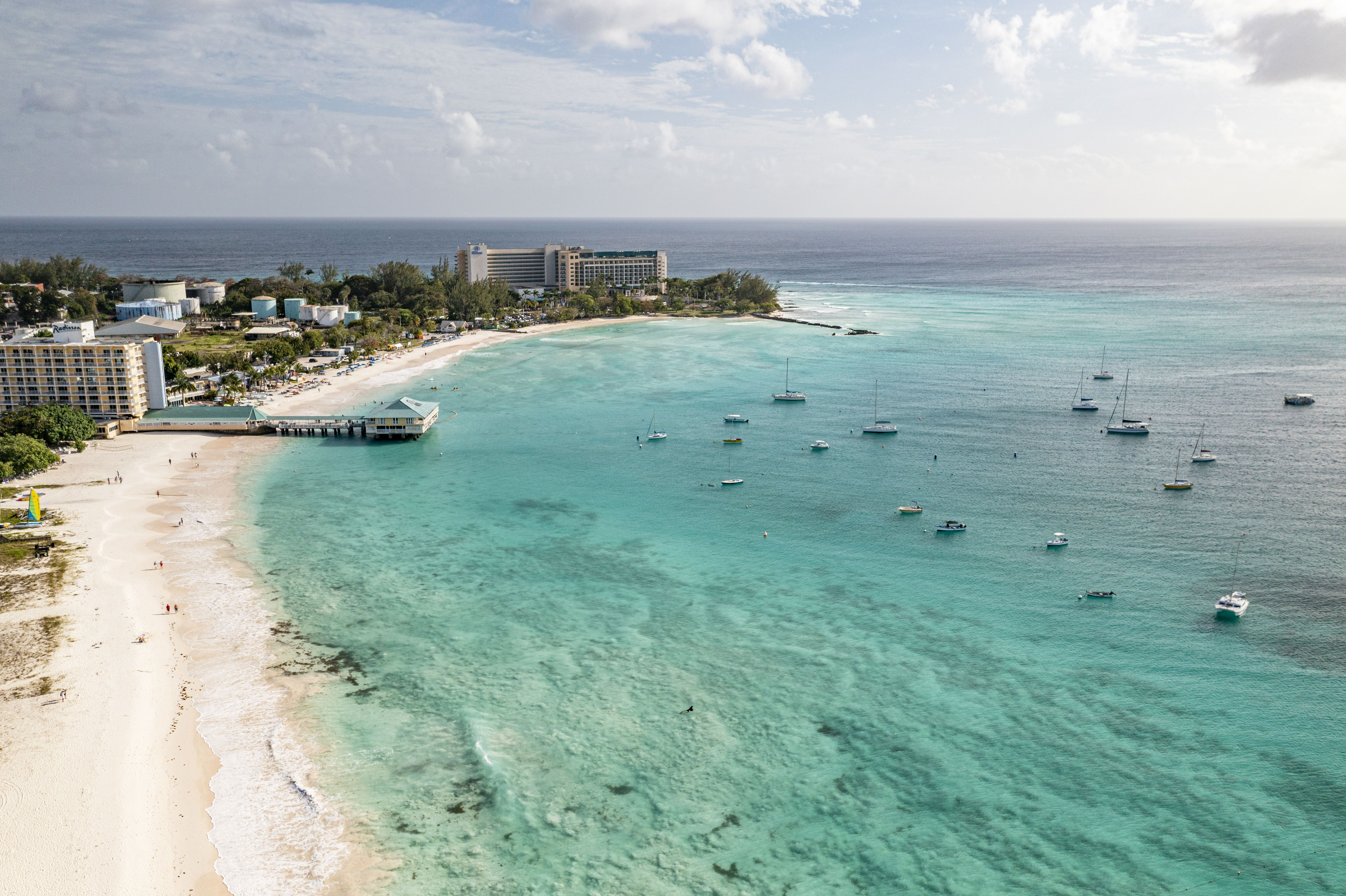 A bay in Barbados with light blue water, hotels, a dock and boats out on the water.