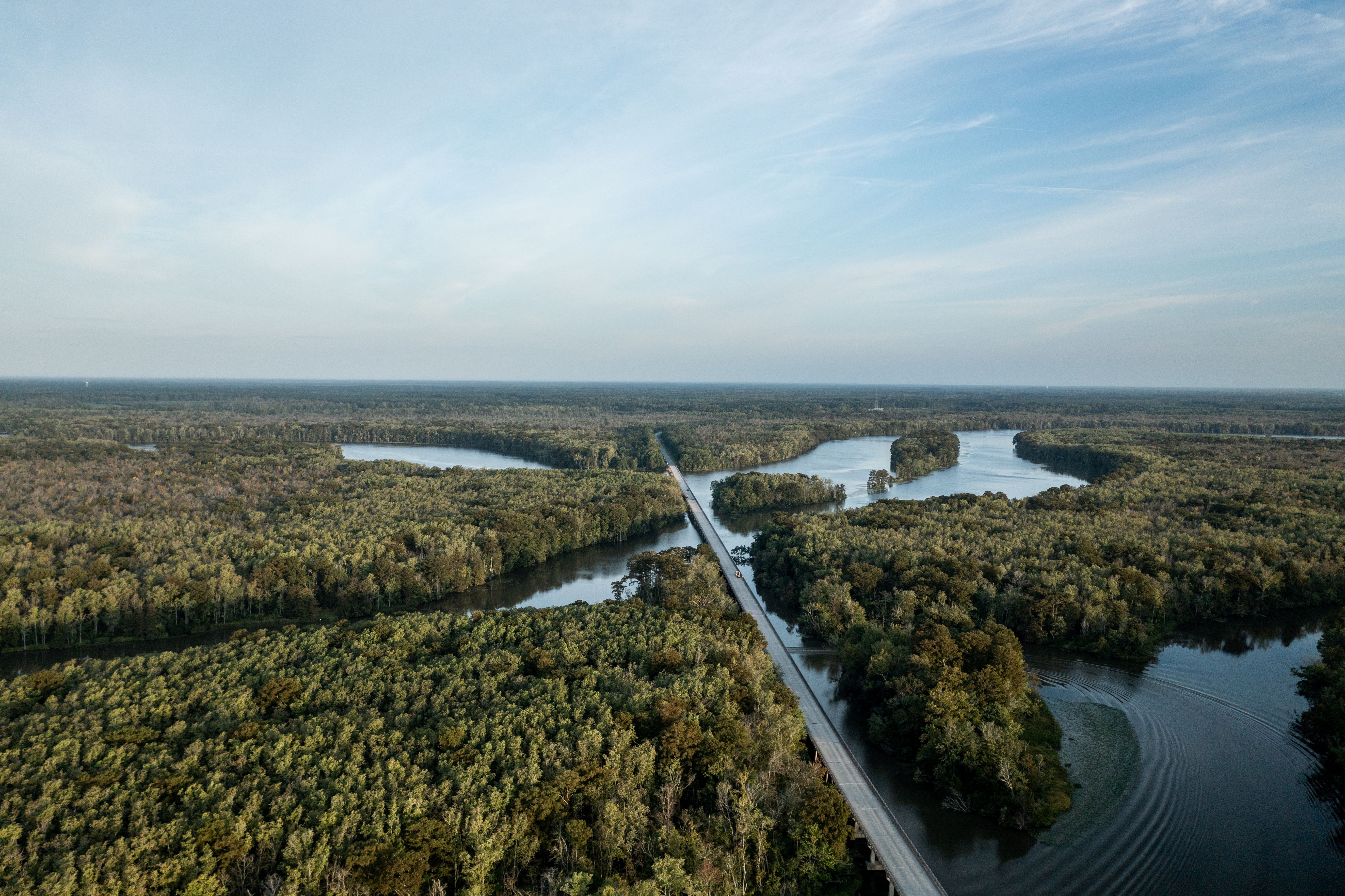 Aerial view looking out over a highway bridge that carries traffic over a river that meanders through a forest.