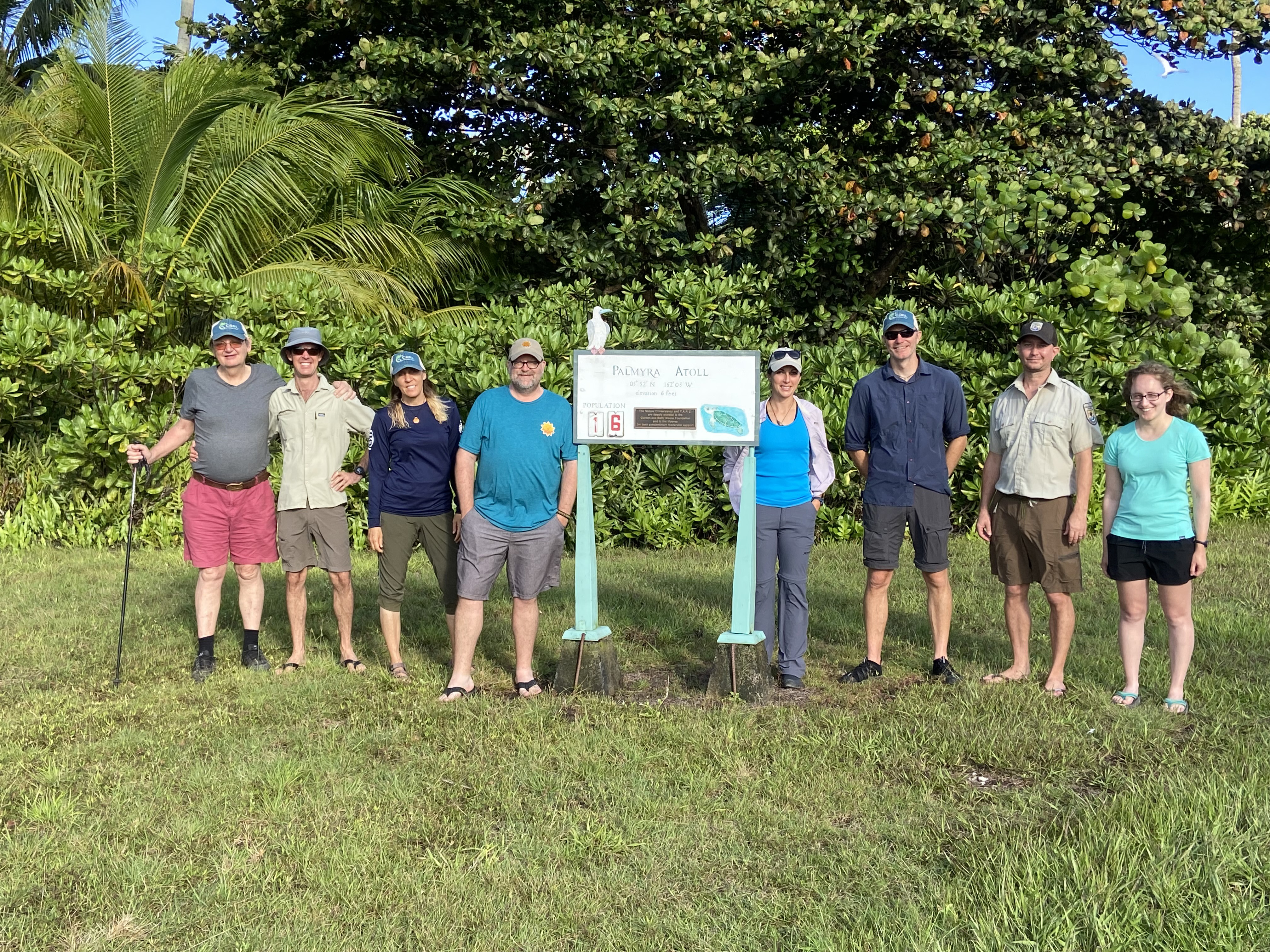 a group of people posing for a picture by a Palmyra Atoll sign.