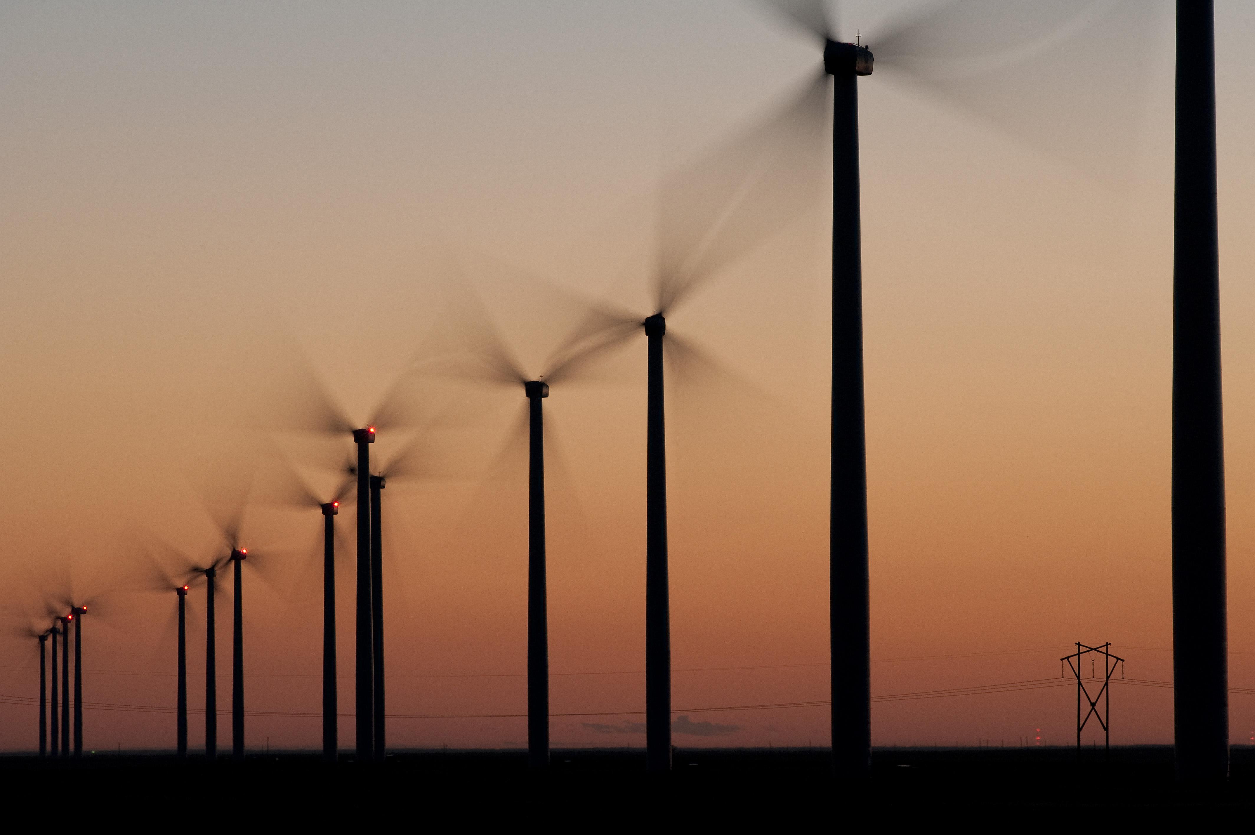 Multiple wind turbines lined up across an evening sky.