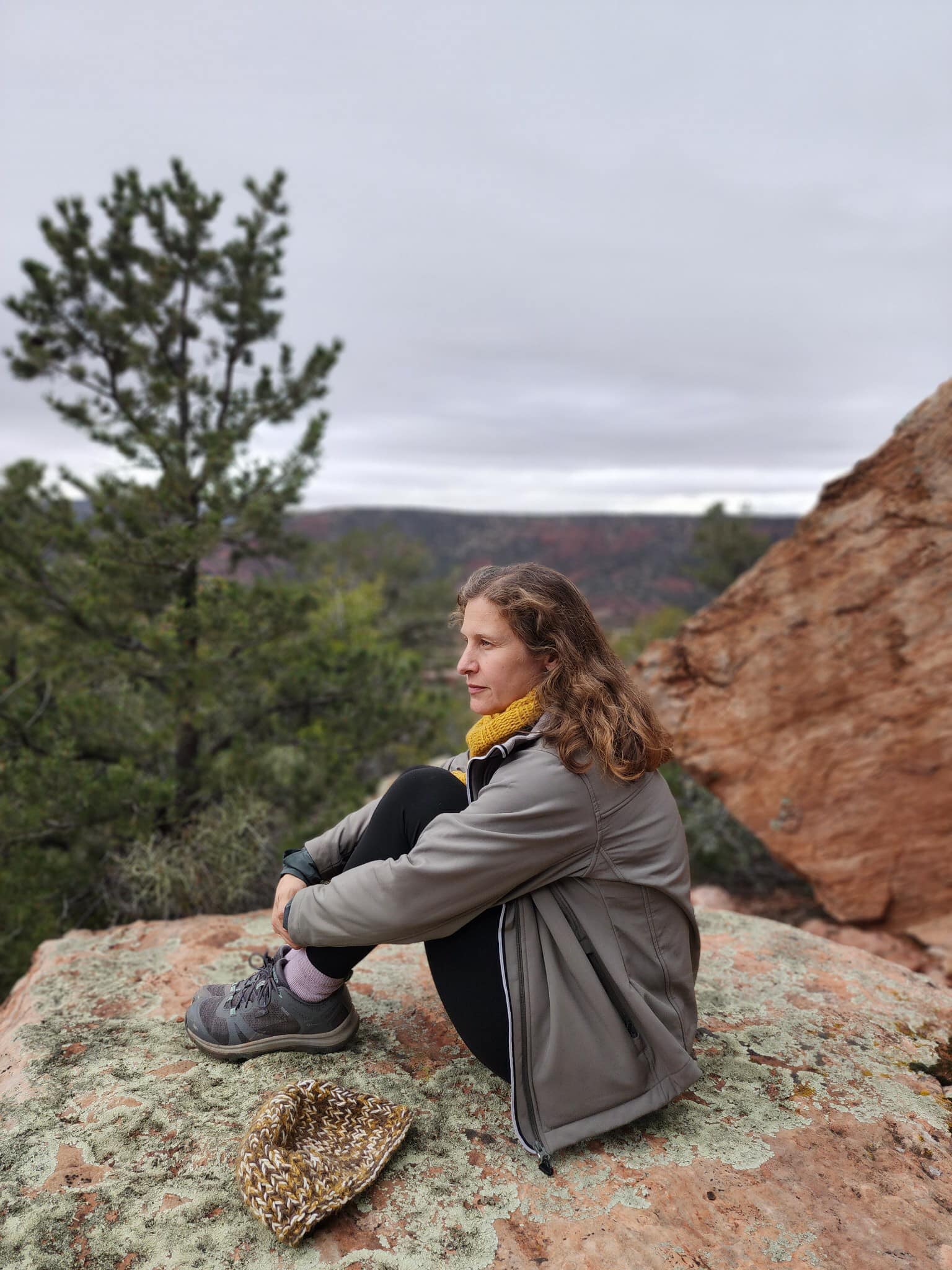 Stephanie Singer sits on rocky cliffside overlooking landscape.
