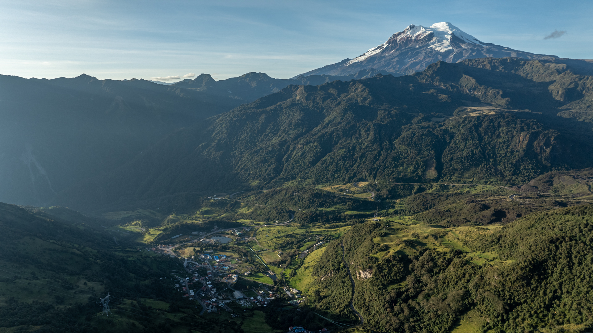 A green field high in a mountainous region, with a snowcapped peak in the background.