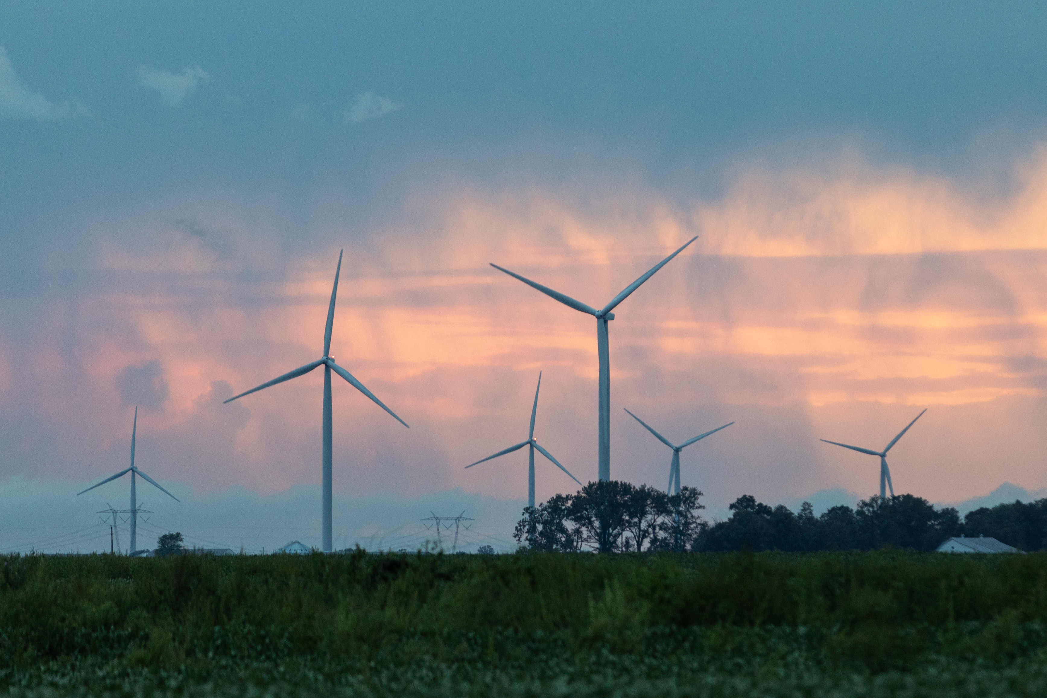 Wind turbines spin against a pink sky.