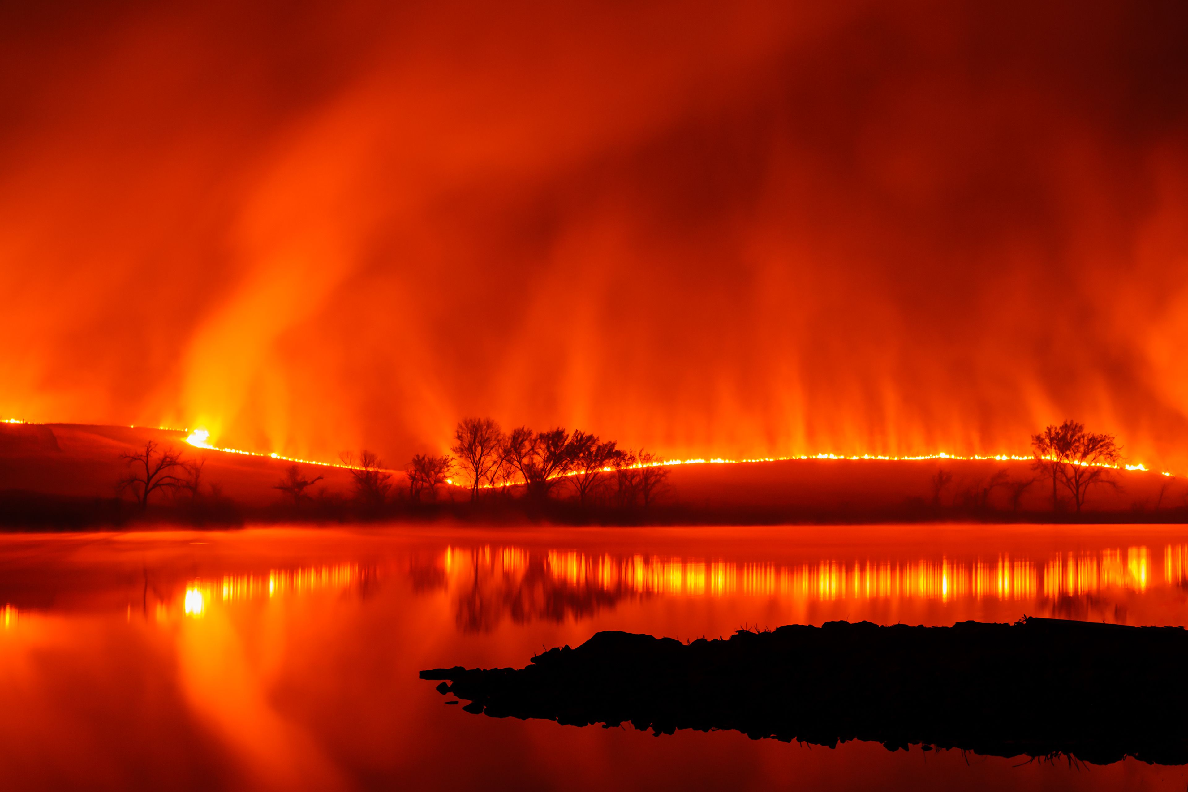 Fire moves across rolling hills as water from Chase Lake reflects flames.