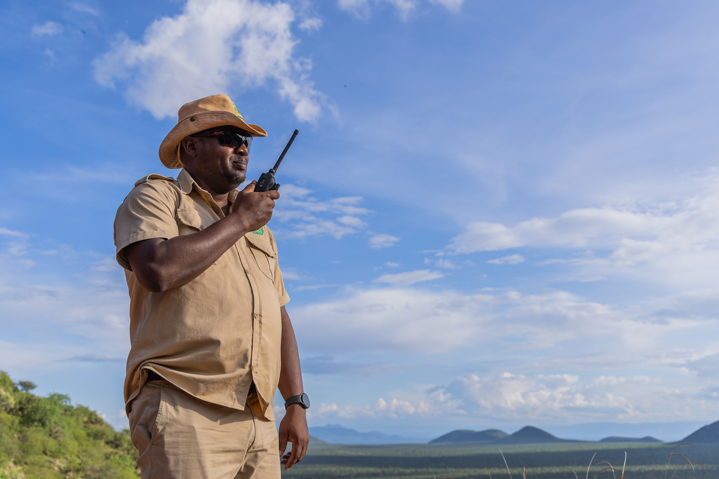 Tomm Lolosoli stands outside and speaks into a walkie talkie.