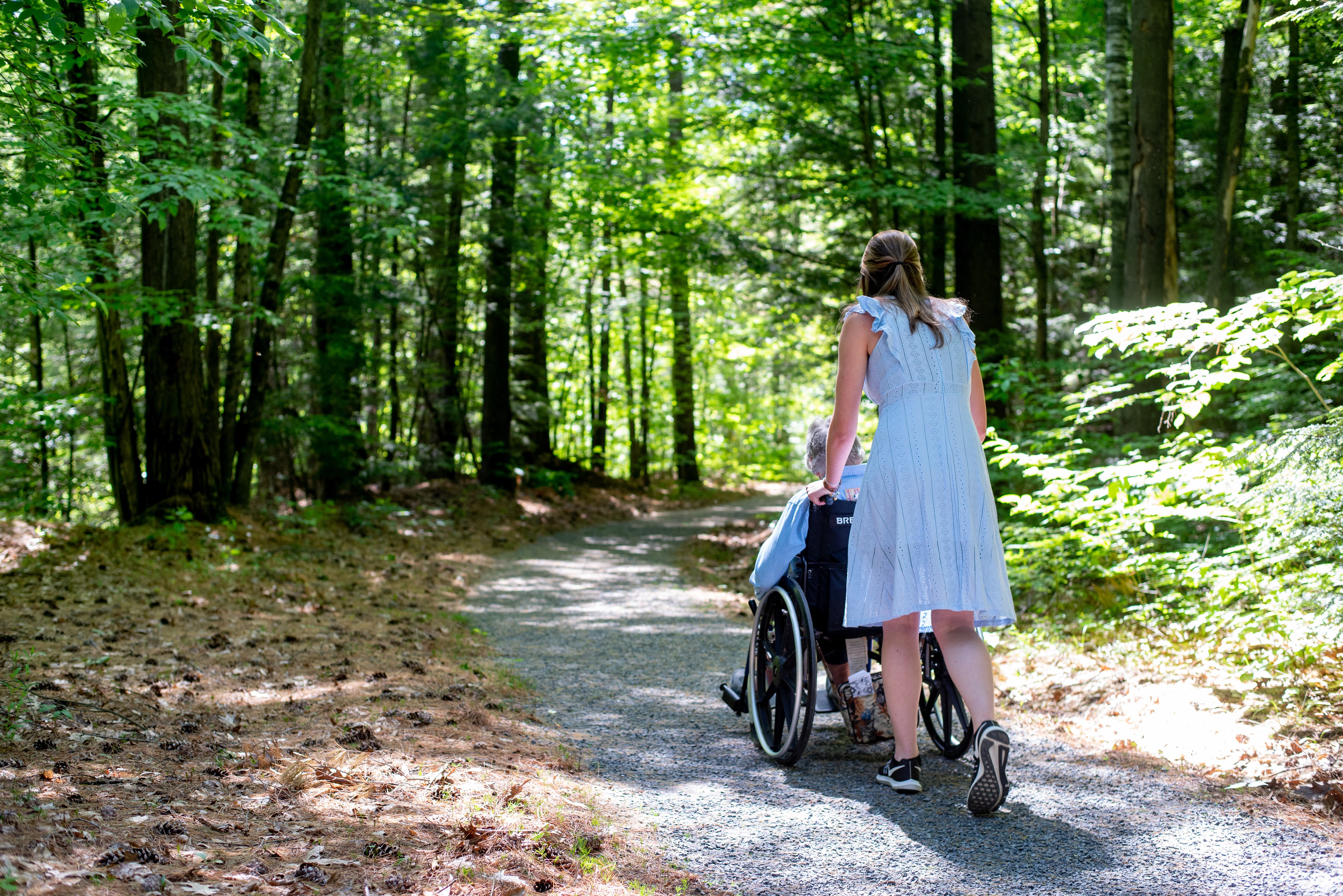 A woman pushes another woman in a stroller down a path.