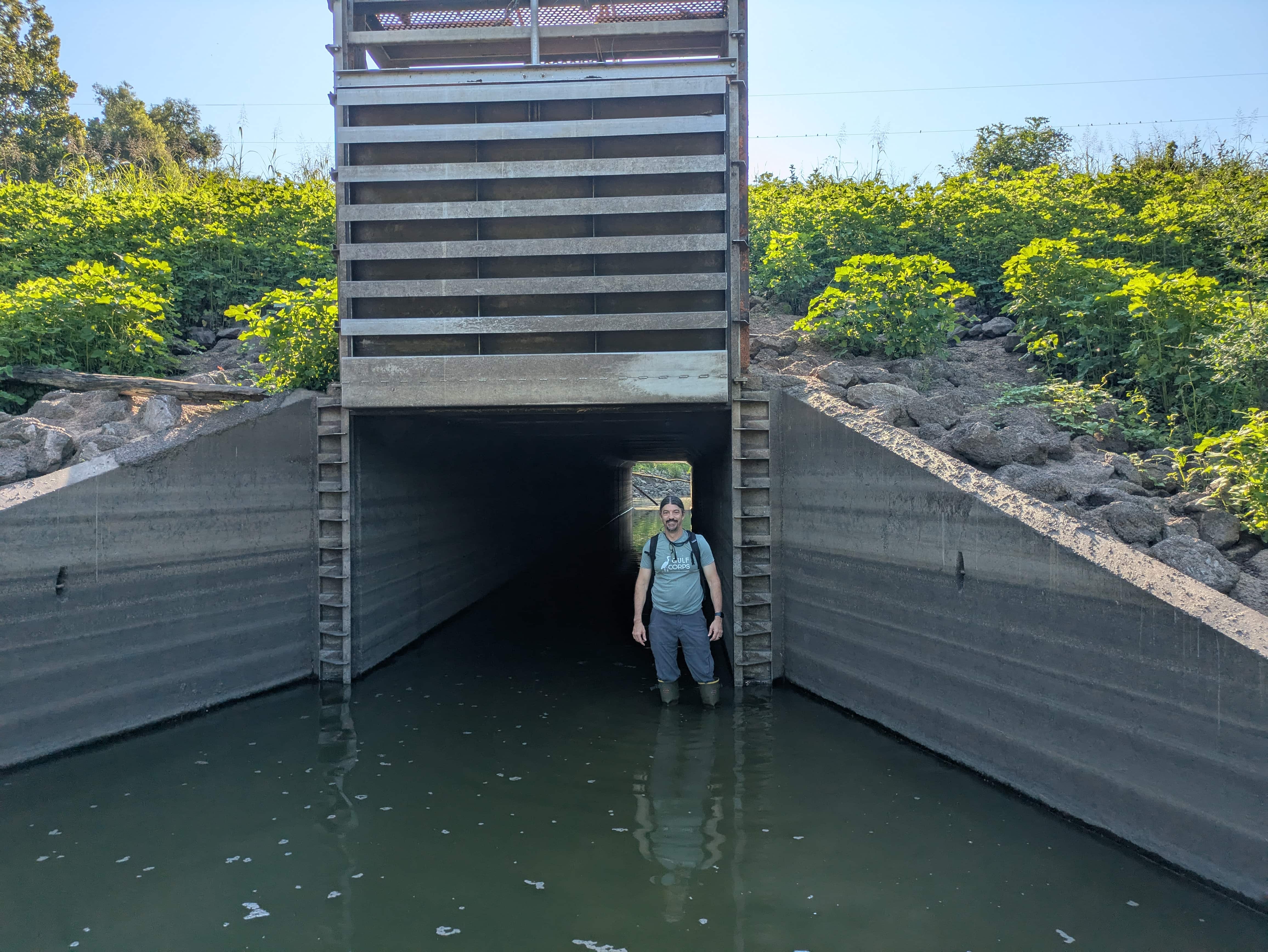 A man stands in water outside of a drainage structure.