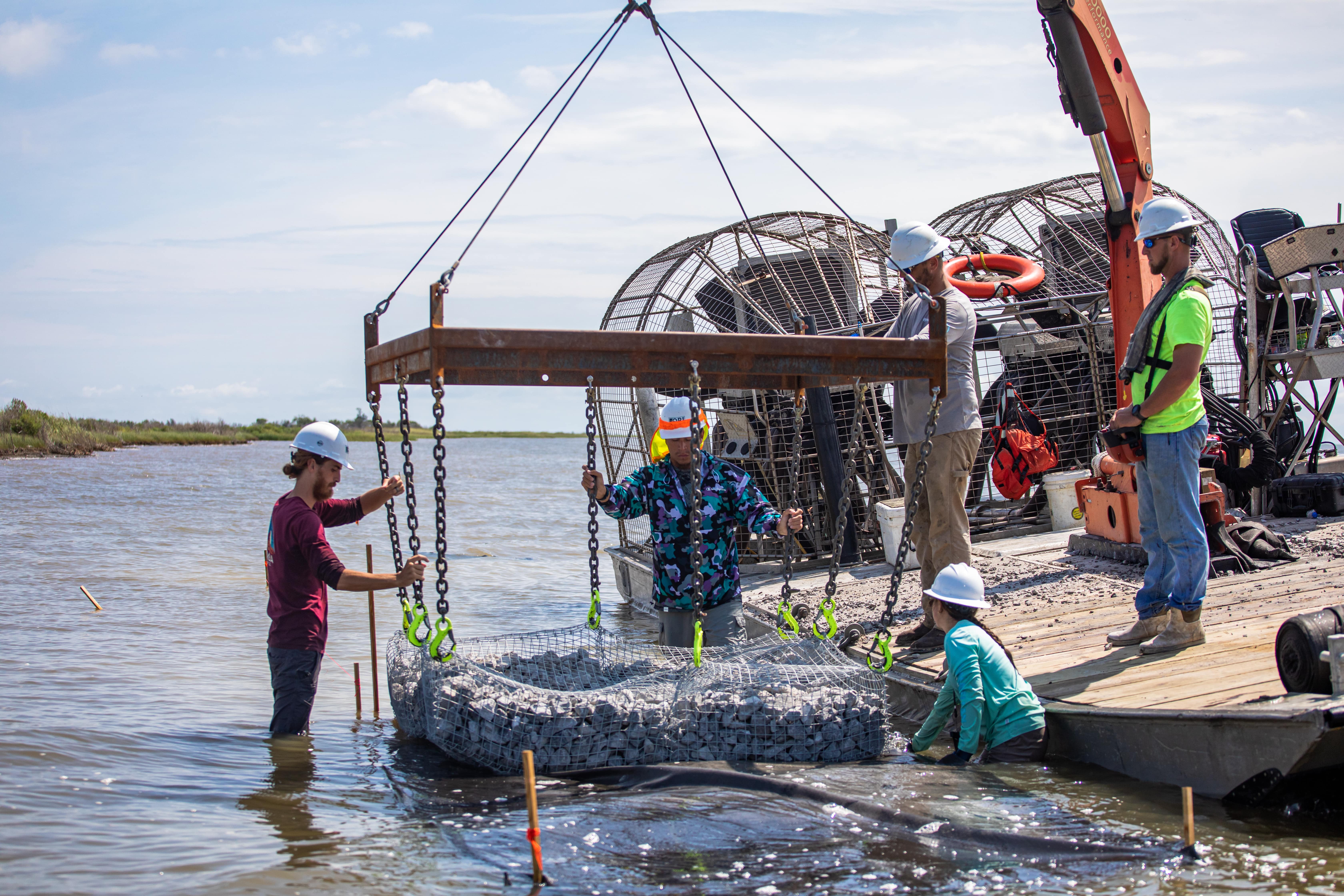 Several people operate machinery situated on a body of water.