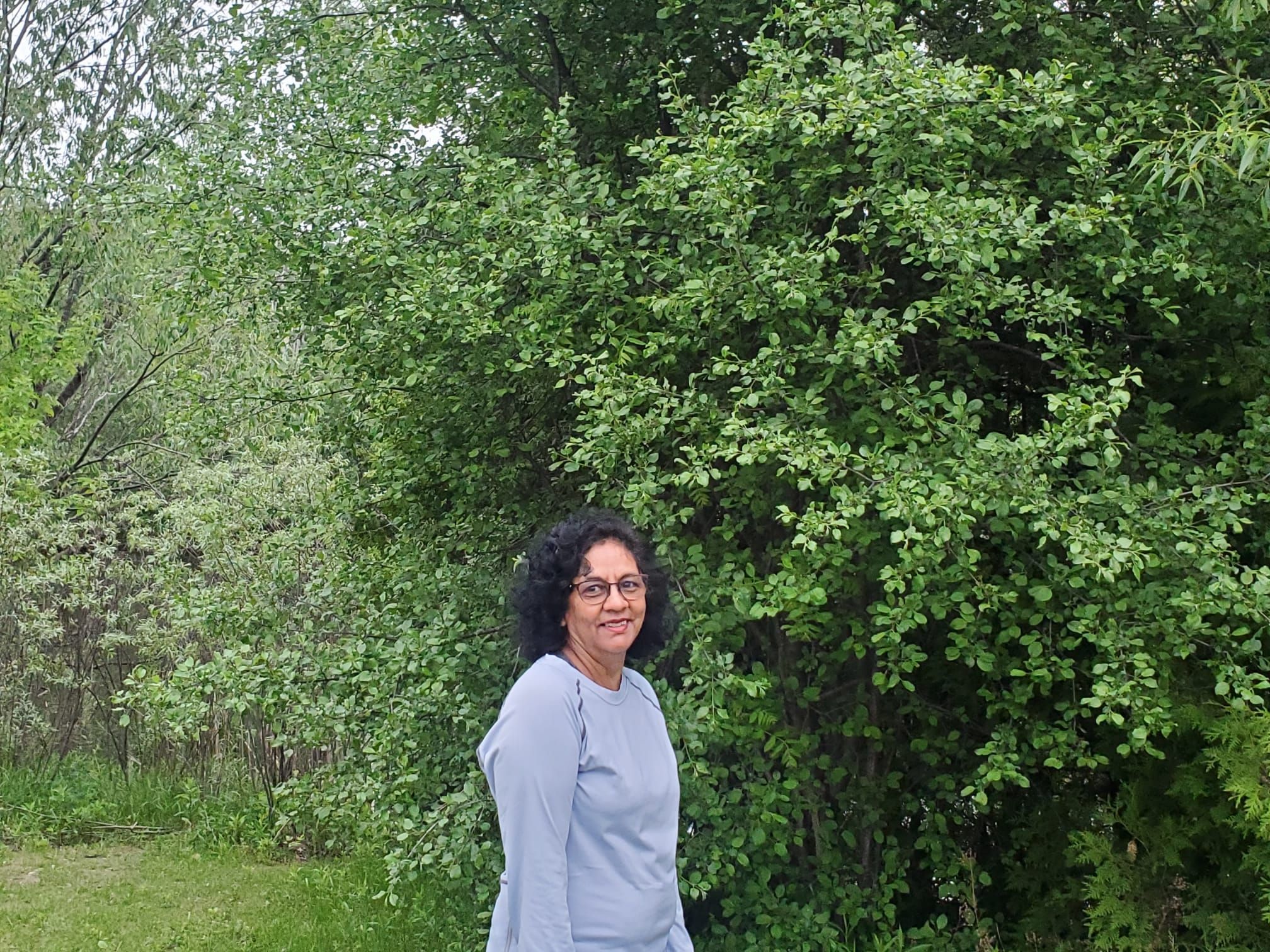 Candid portrait of Basmati Persaud standing outside near trees.
