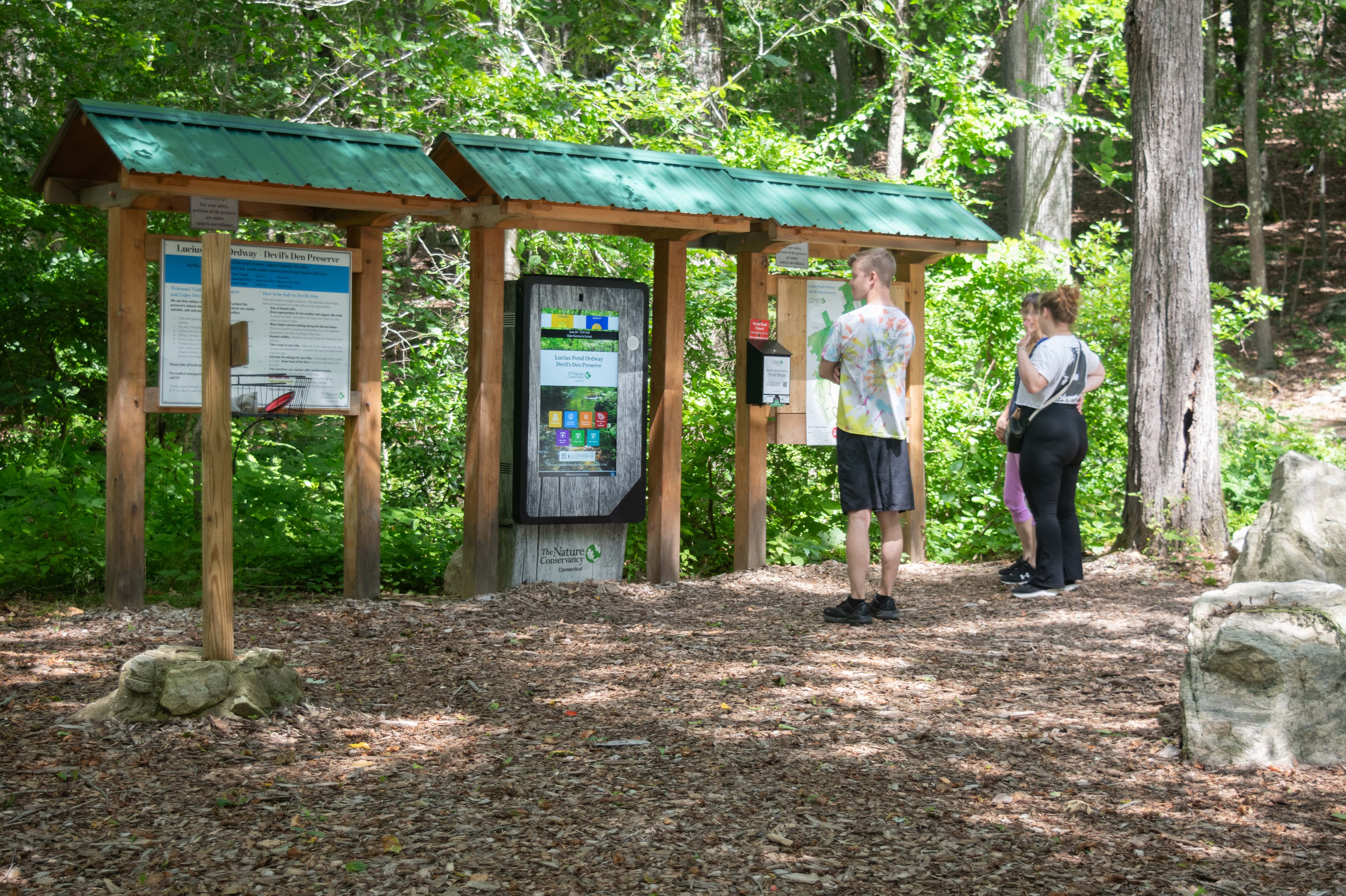 People stand in front of a kiosk surrounded by a forest.