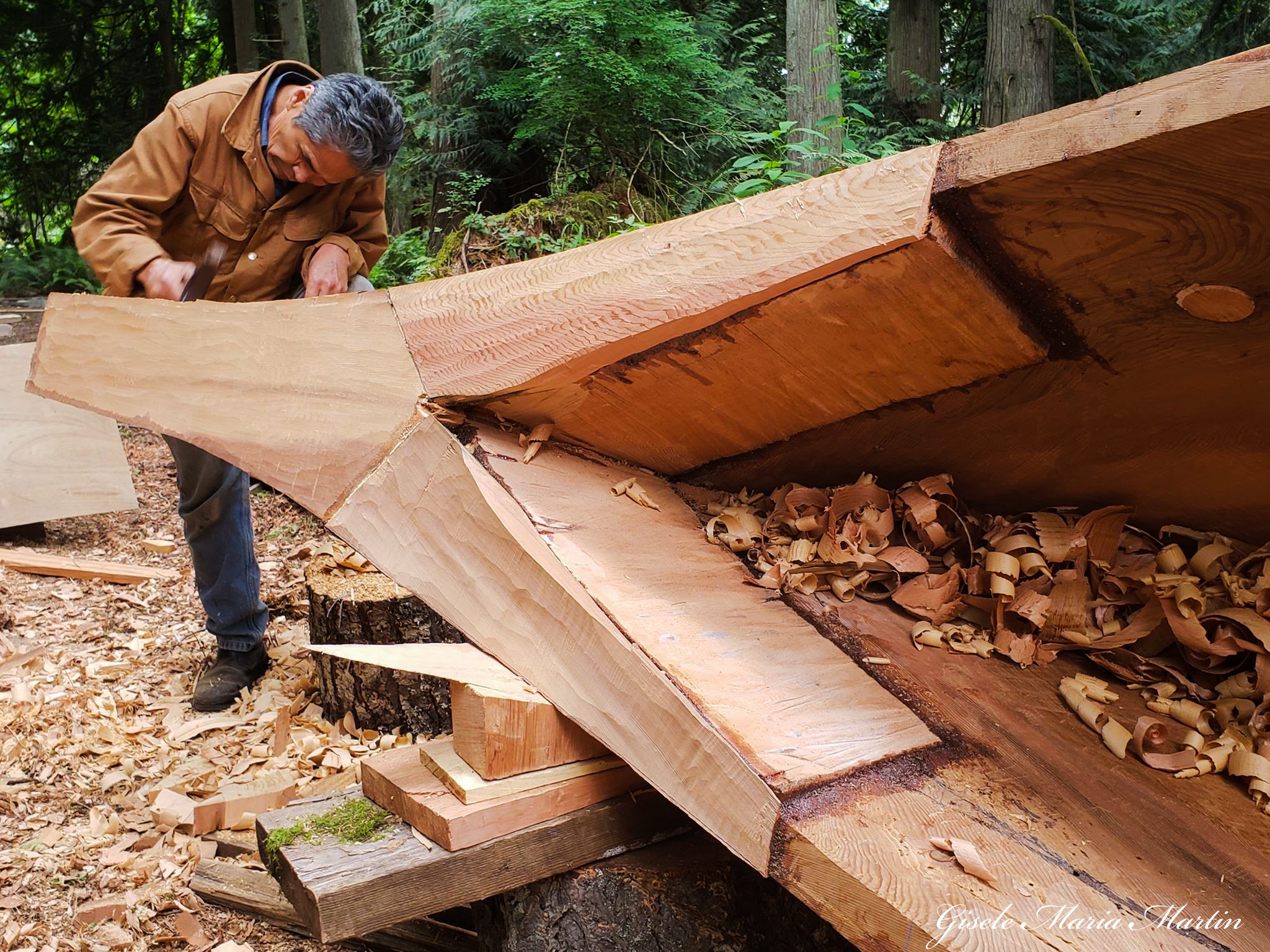 A person carving a canoe lying sideways as they work on the front or back of the vessel.