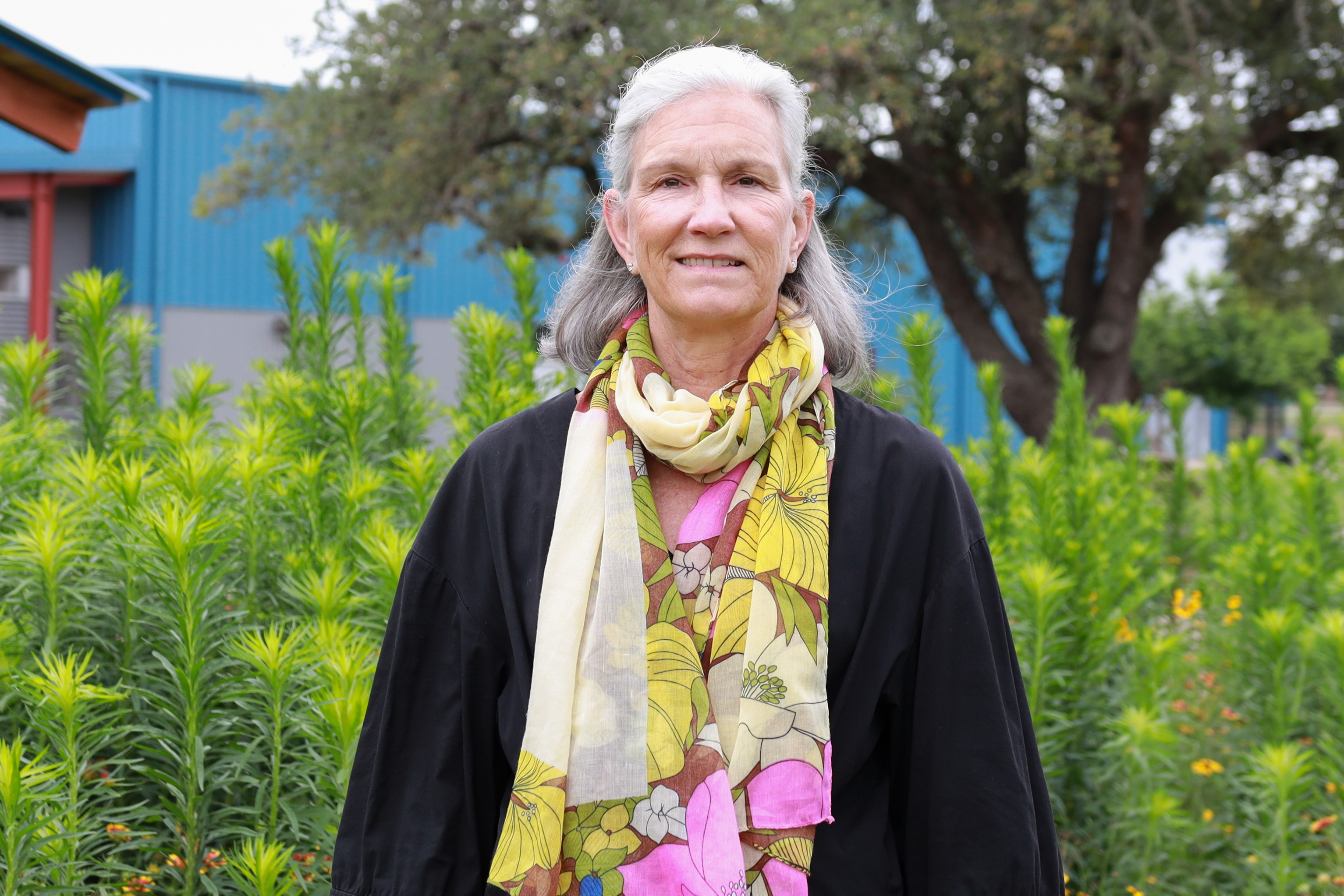 A woman stands in front of tall green plants.