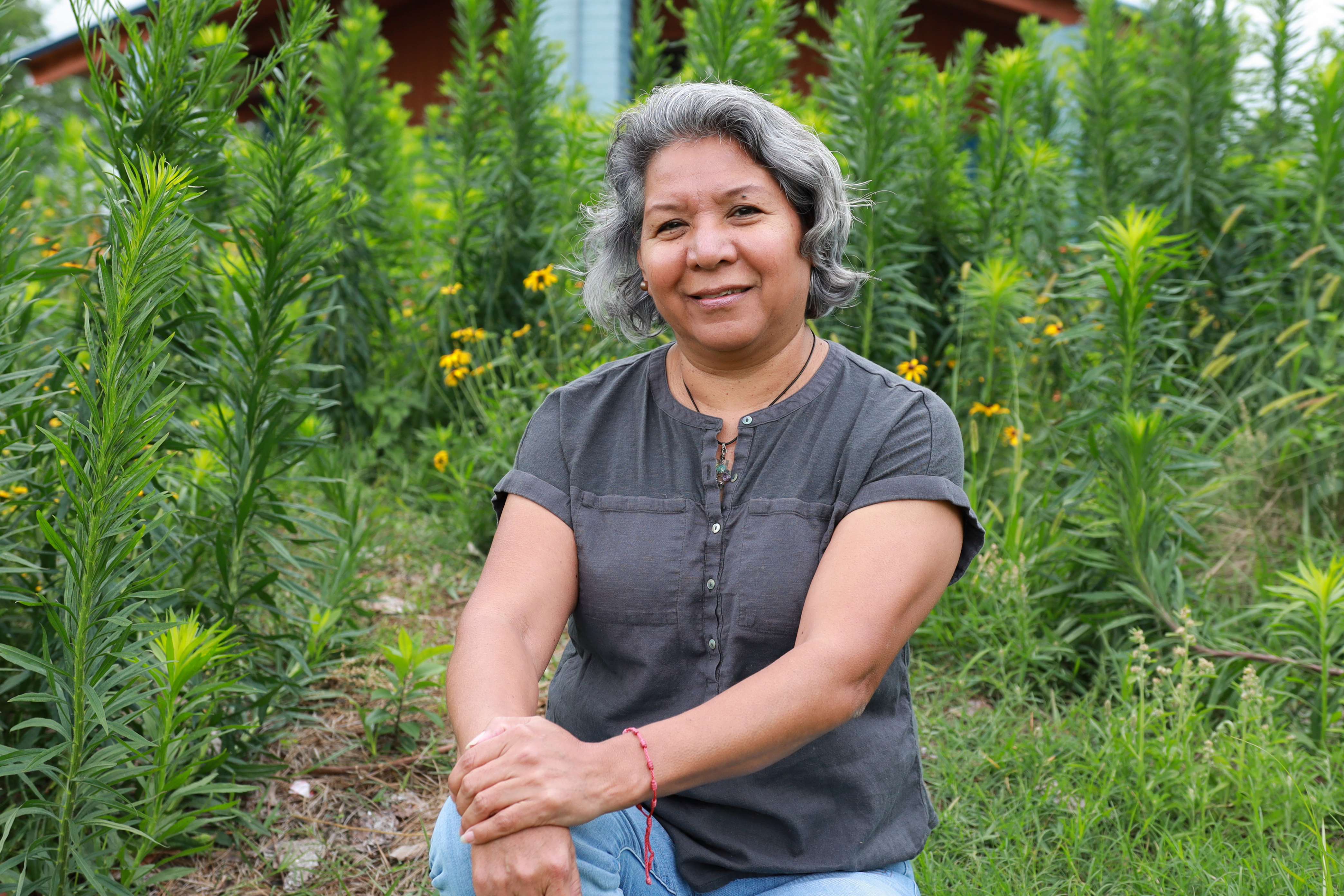 A woman sits in a field of green plants and flowers.