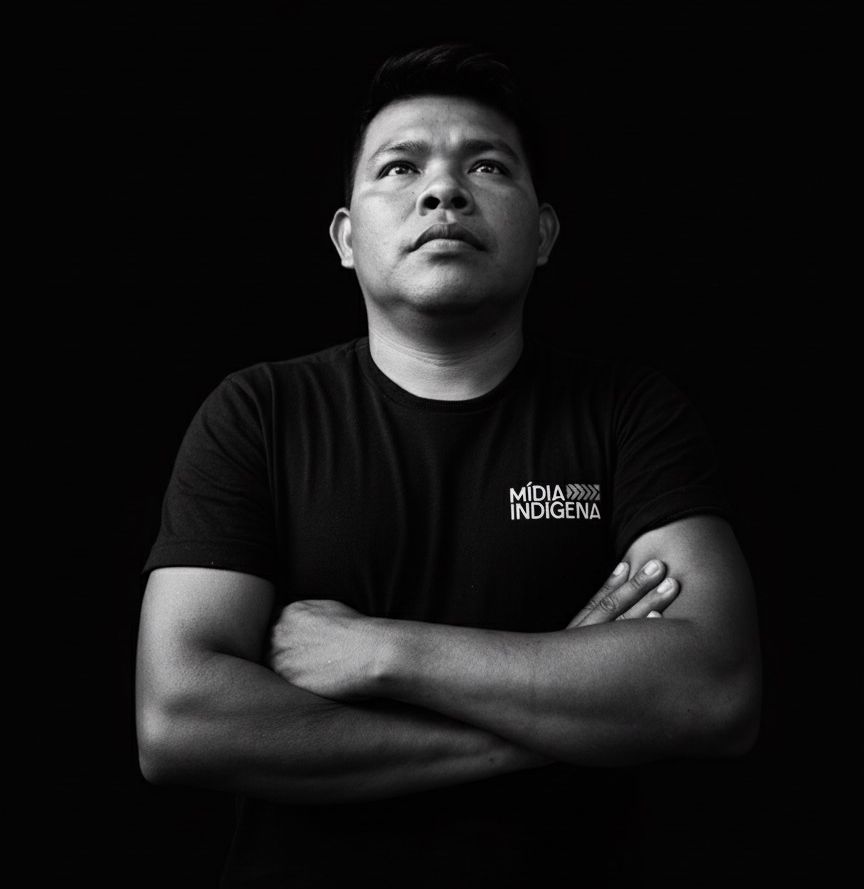 Black and white portrait of Kawowe Parakana, with a black t-shirt, arms crossed and looking up with serious expression. 