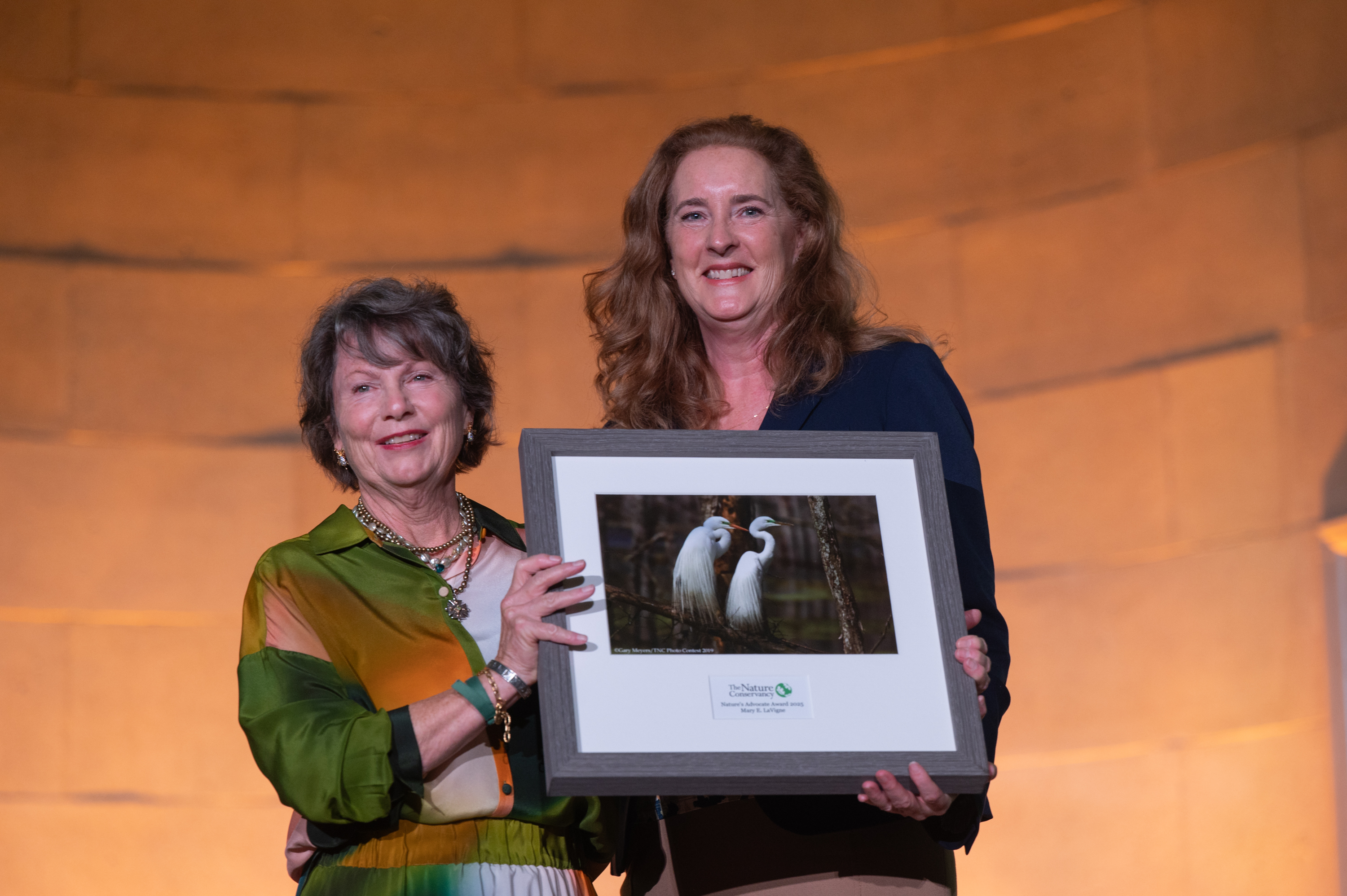 Two women stand holding a photo of birds between them. 