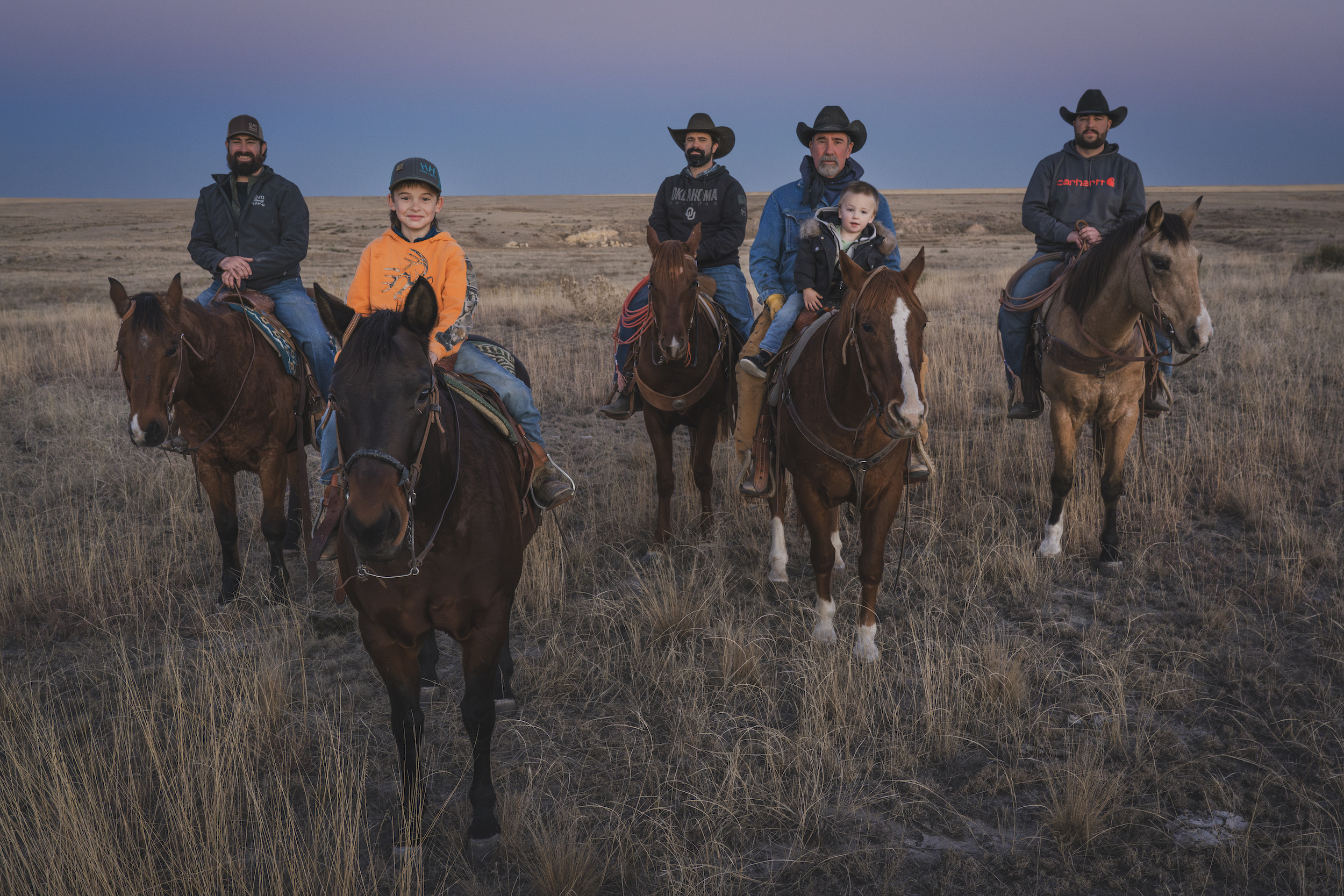 Ranchers on horses look at camera. 