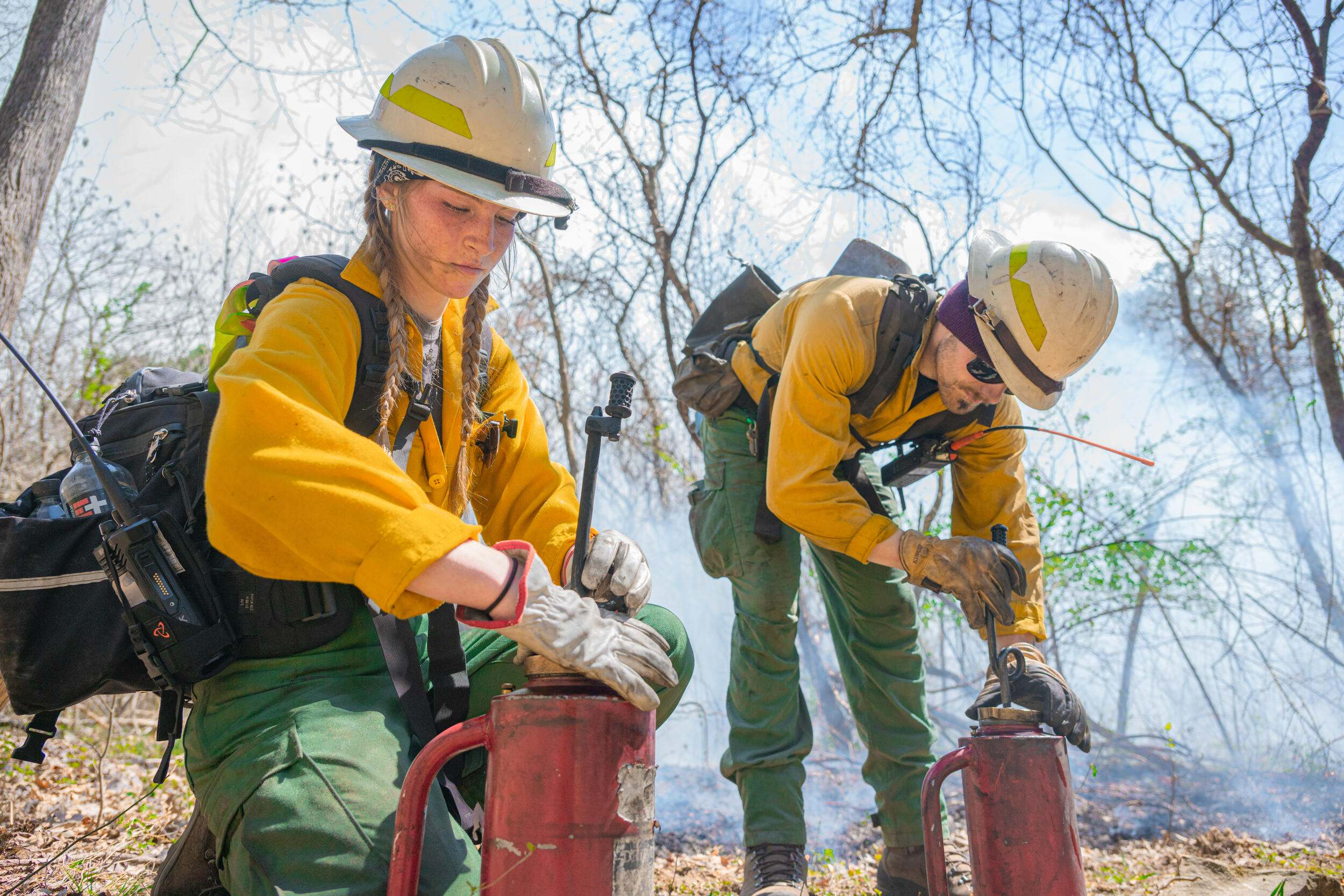 Two women dressed in yellow fire gear preparing their tools for a prescribed fire. 