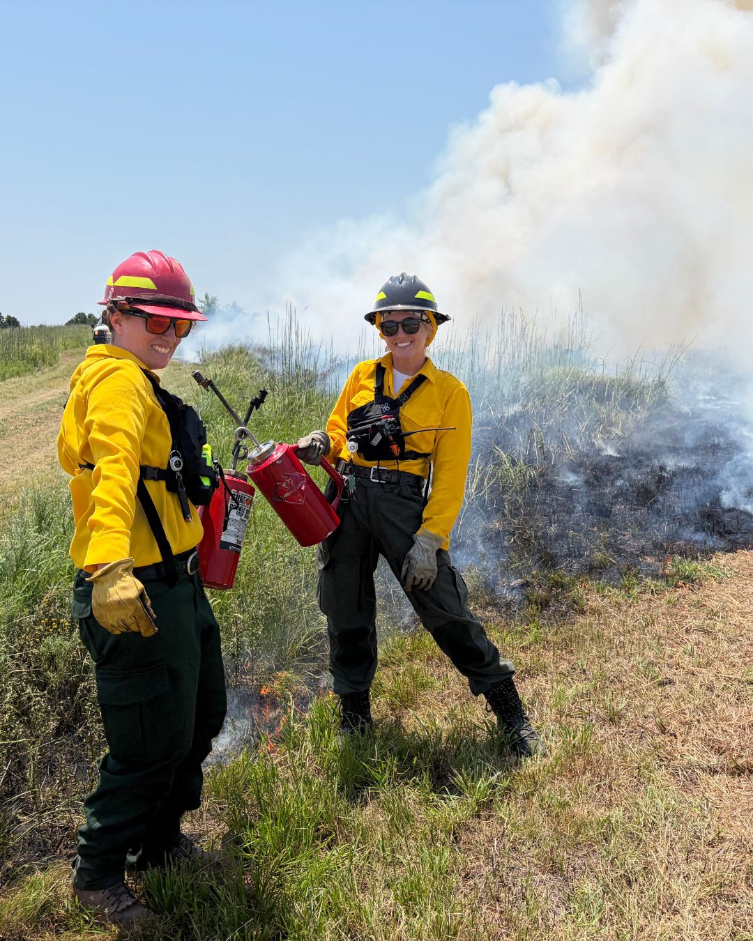 TNC fire crew smiling at the camera with their drip torches and smoke rising out of the grasslands behind them.