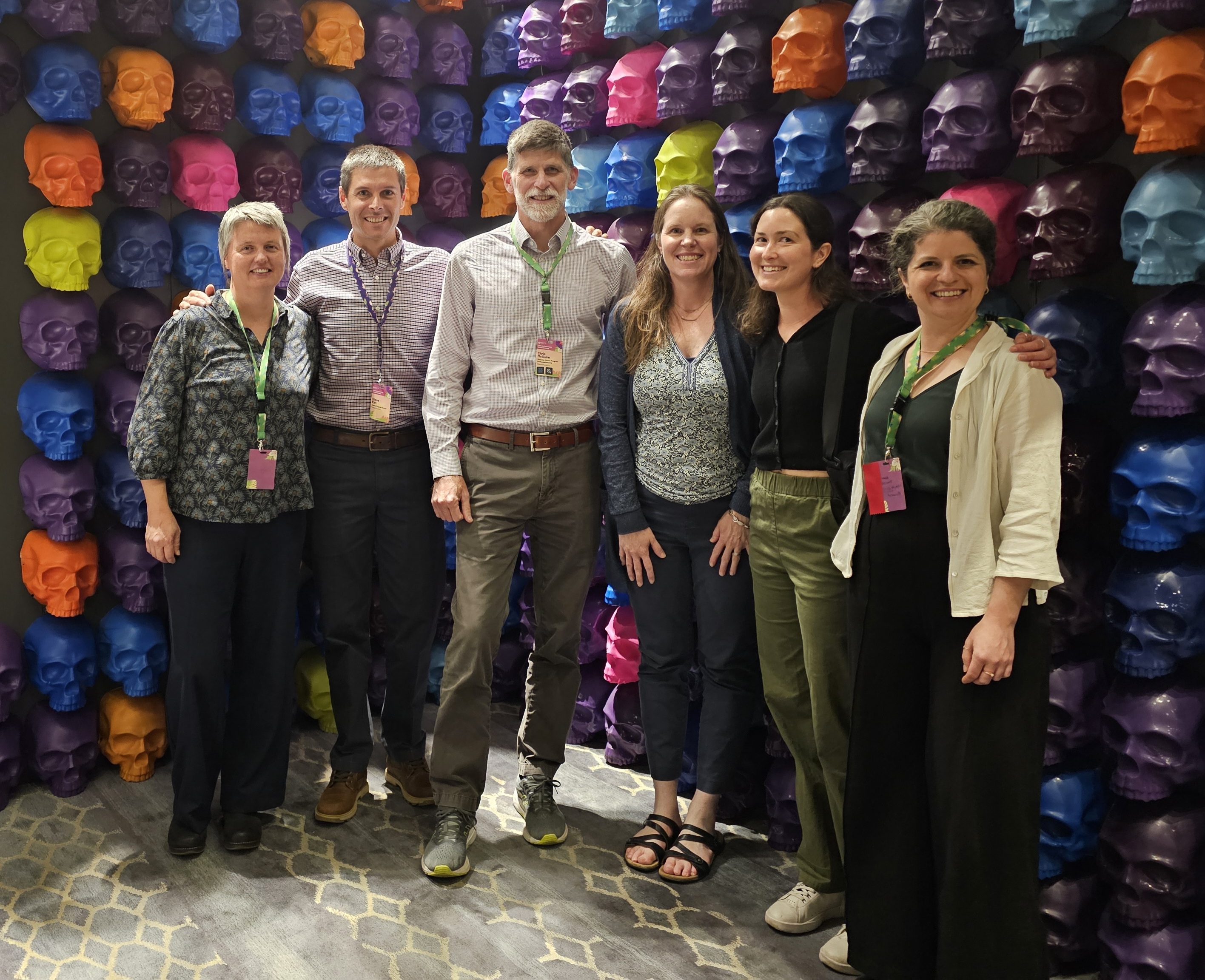 A group of scientists from Massachusetts poses in front of a wall decorated with colorful skulls at the TNC Global Science Gathering in Mexico City.