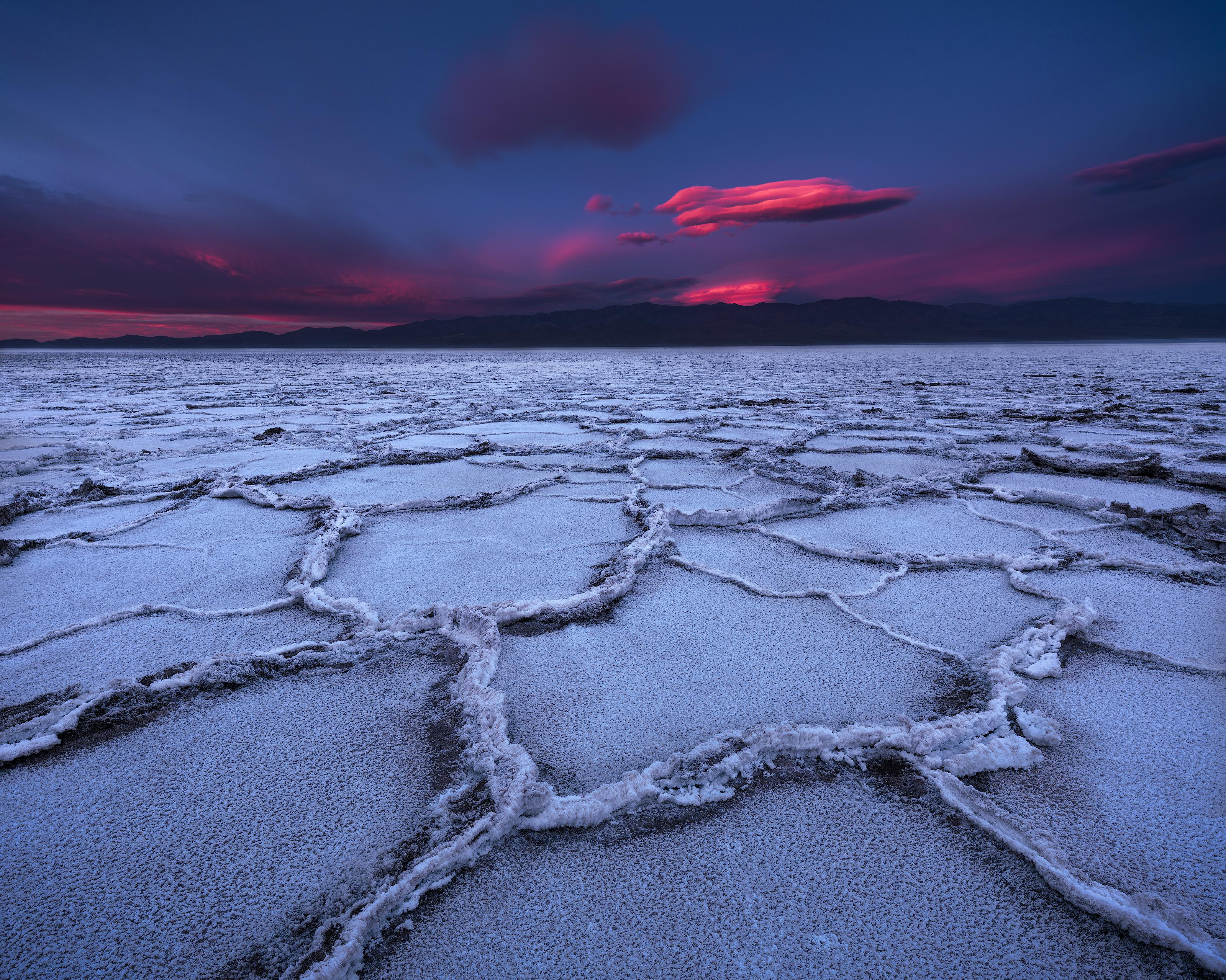 Vista a nivel del suelo de un salar en forma de mosaico en el Valle de la Muerte, con un cielo espectacular resaltado por vibrantes nubes rosas.