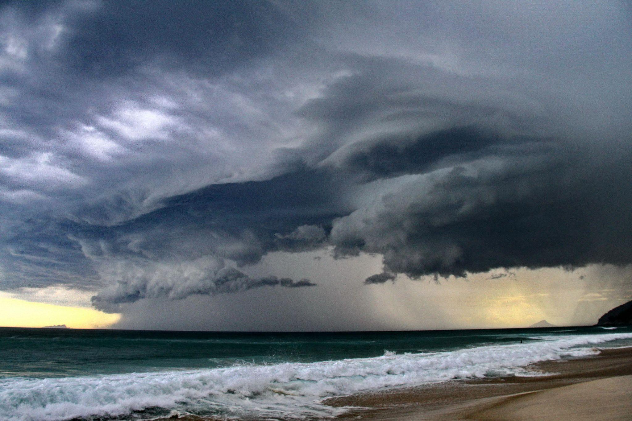 Vista panorámica de una playa y de la costa con espectaculares nubes de tormenta grises en lo alto y láminas de lluvia cayendo sobre el océano a lo lejos.