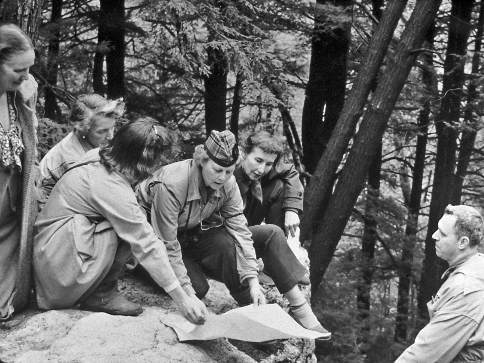 Black and white photo of a group of people looking at a map on a trail. 
