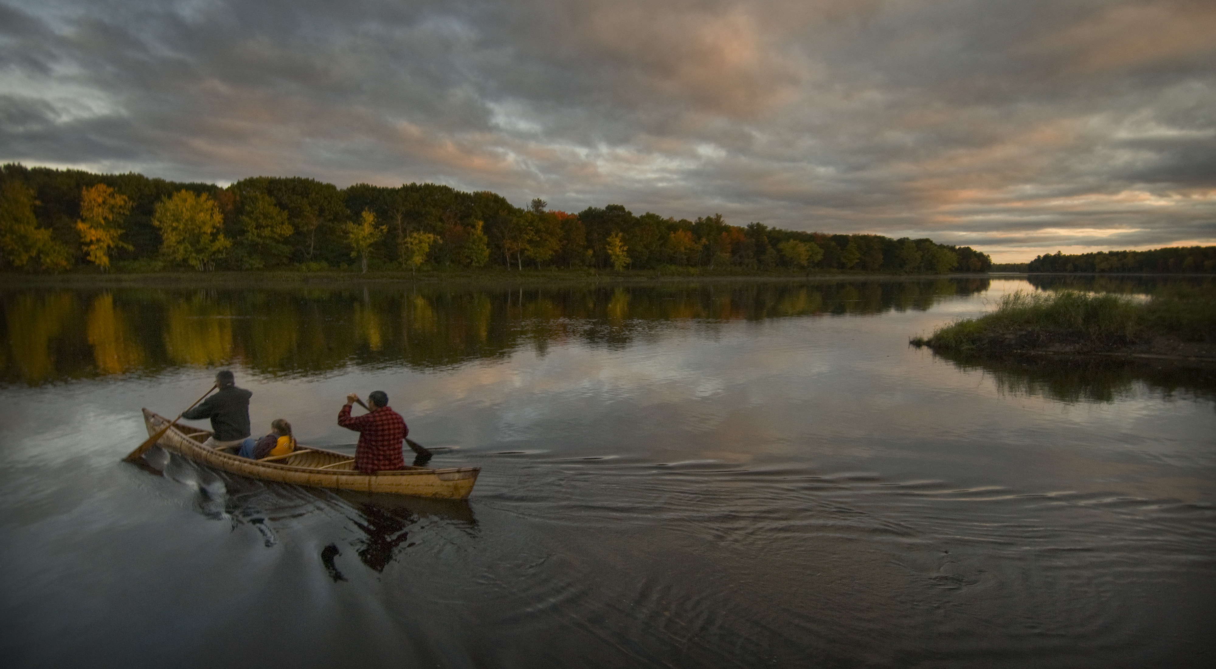 Anciano, adulto y niño reman una canoa en un río.