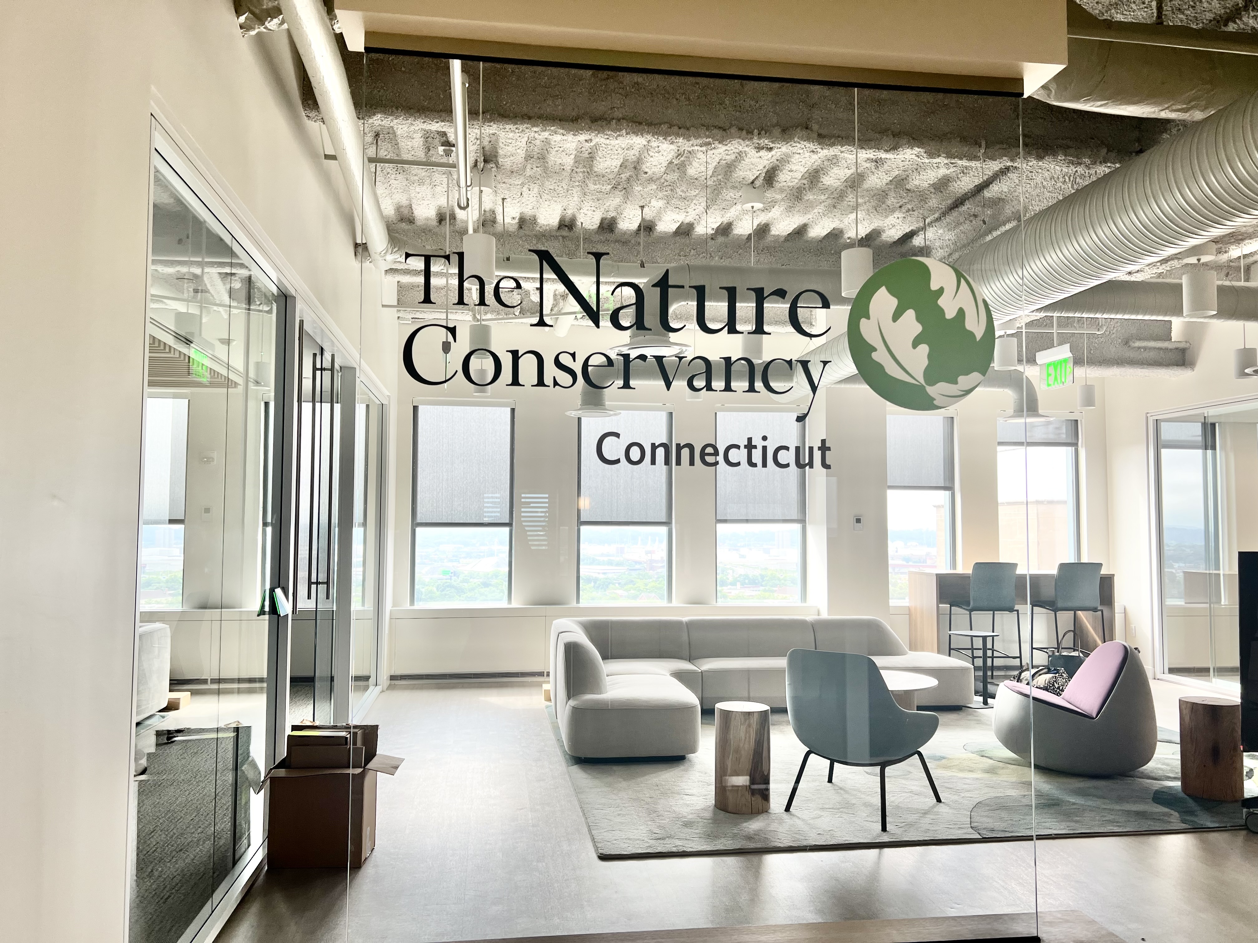 A sunlit office is viewed through a glass Nature Conservancy sign.