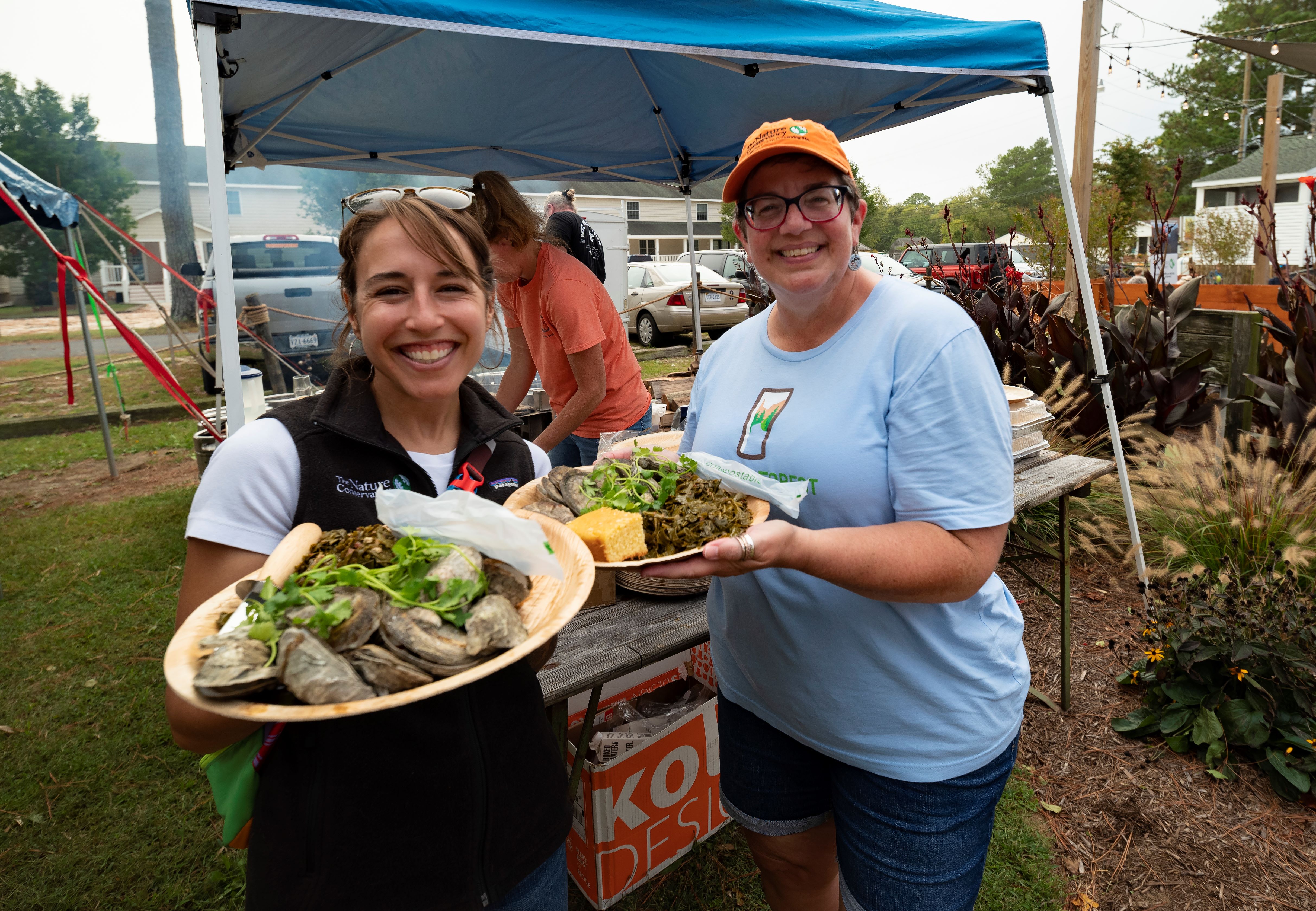 2 women smile and pose with plates heaped with oysters.