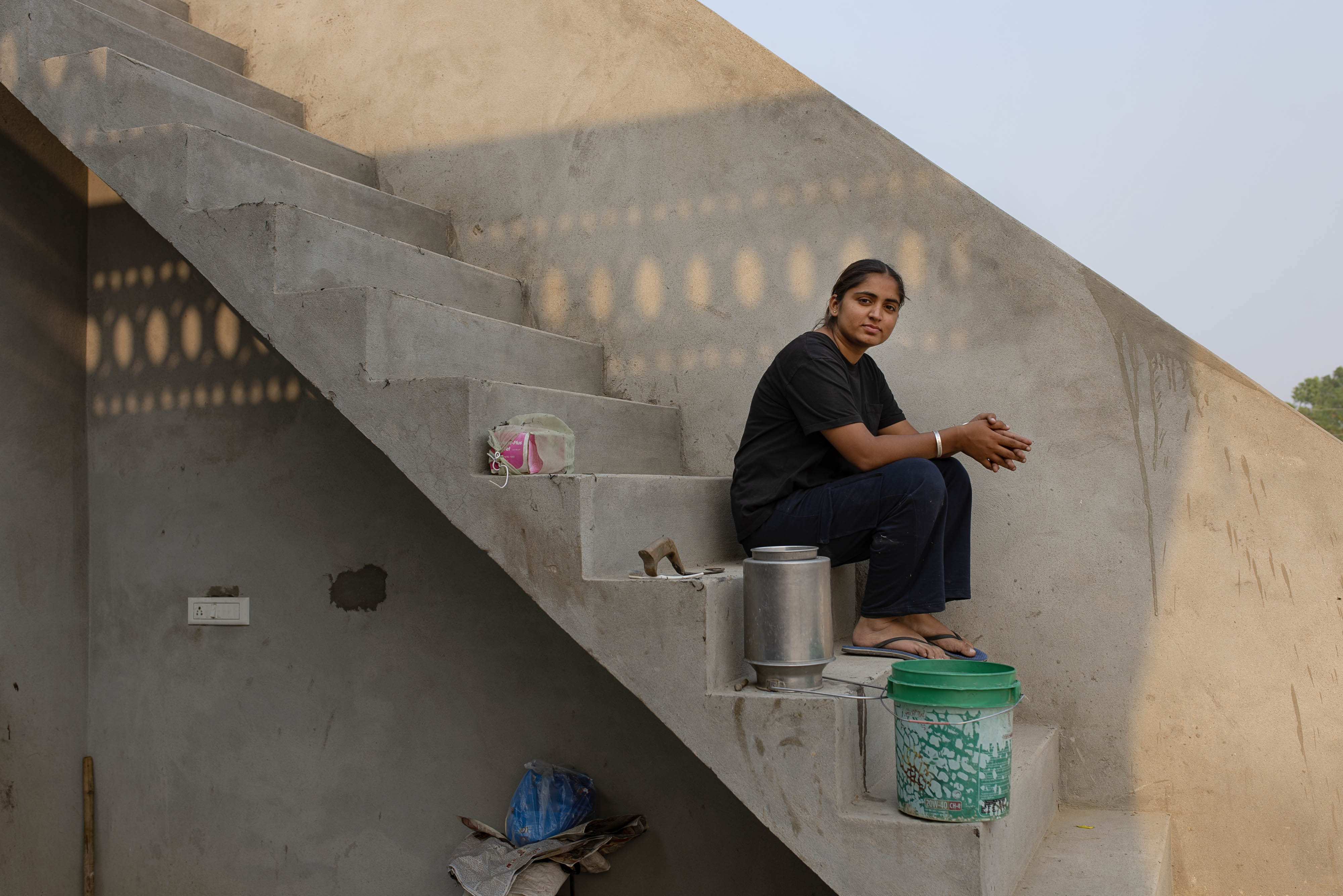 Amandeep Kaur sits on concrete stairs that run along the side of a concrete building.