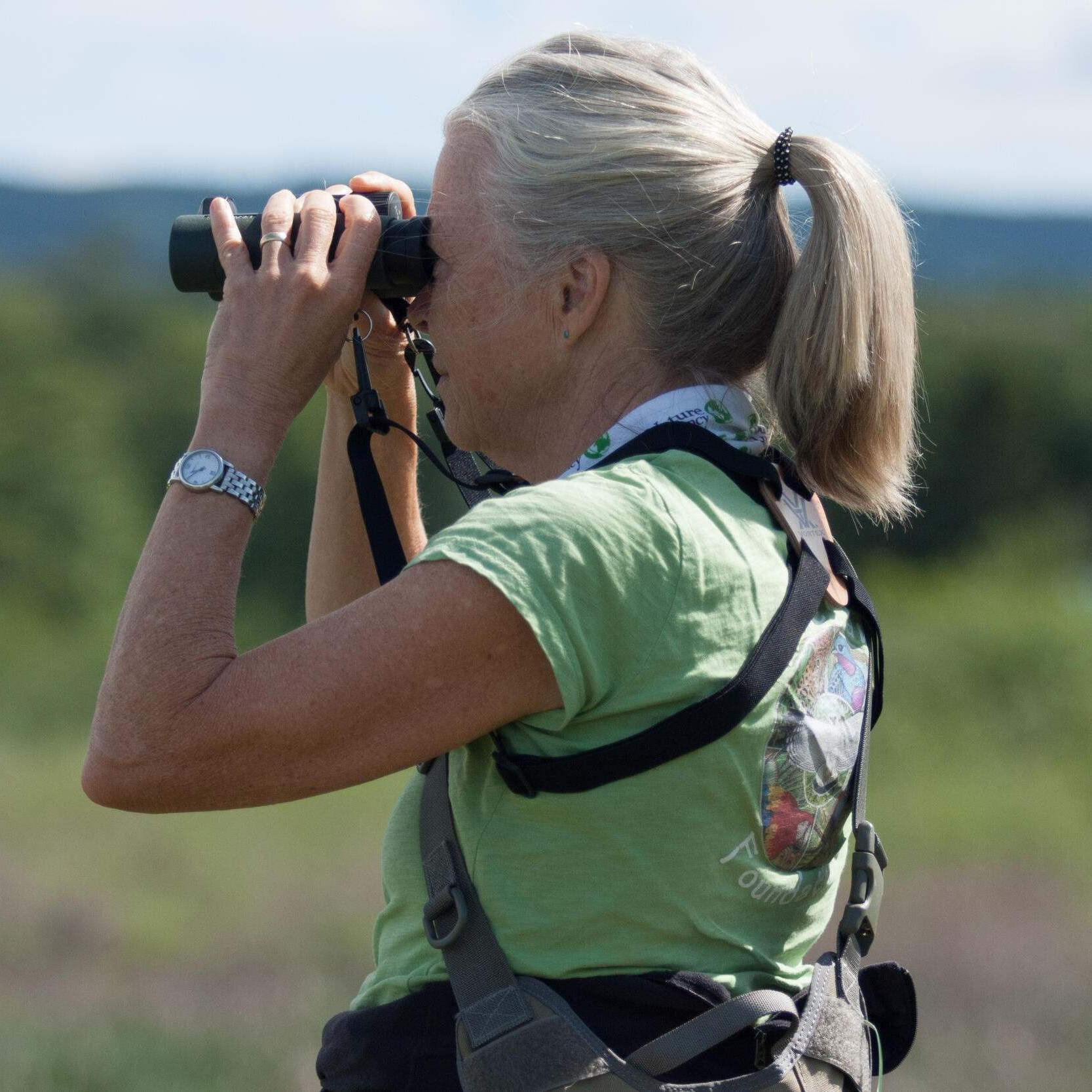 A woman holding binoculars to her eyes.