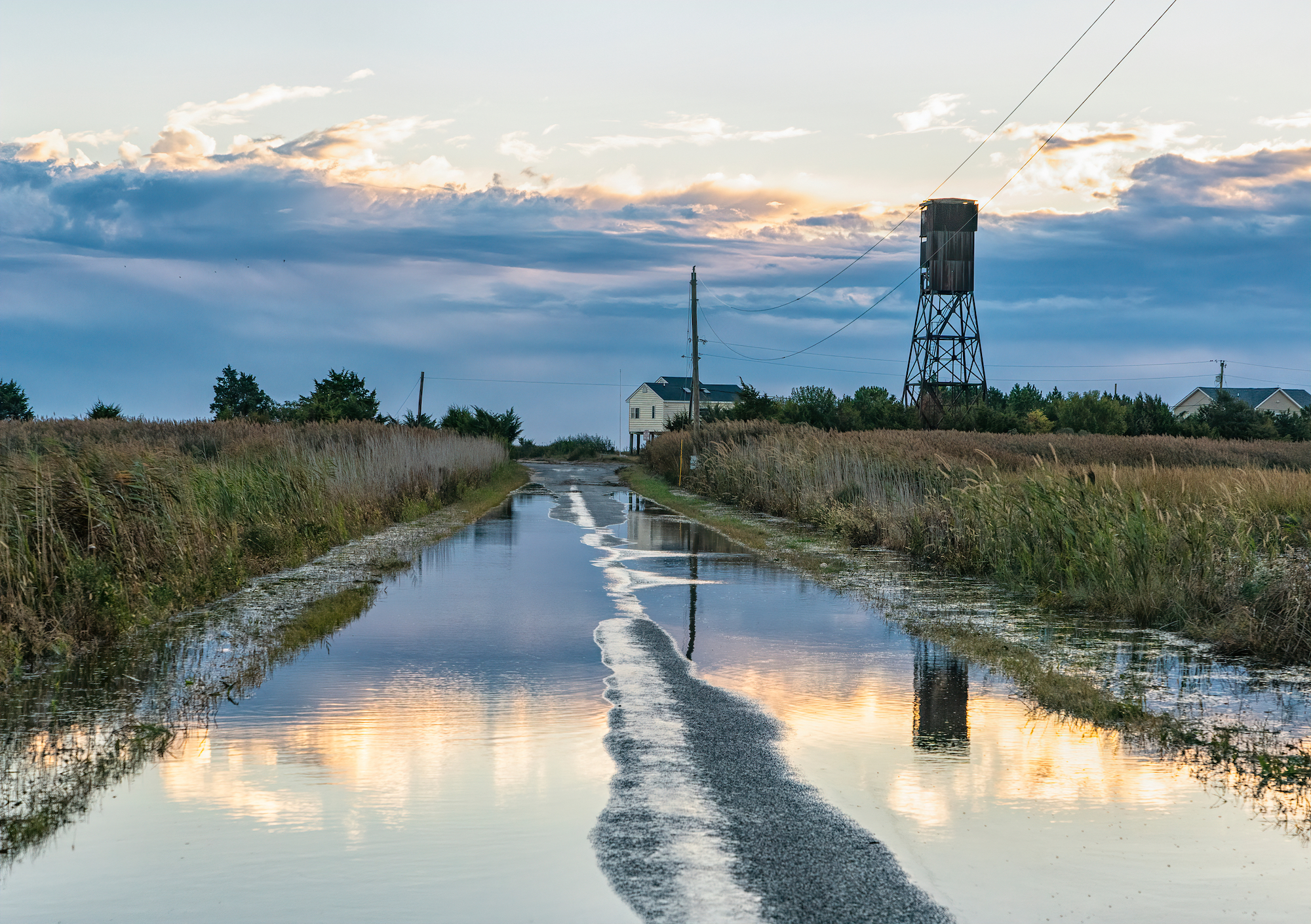 A flooded road leads to farm buildings.