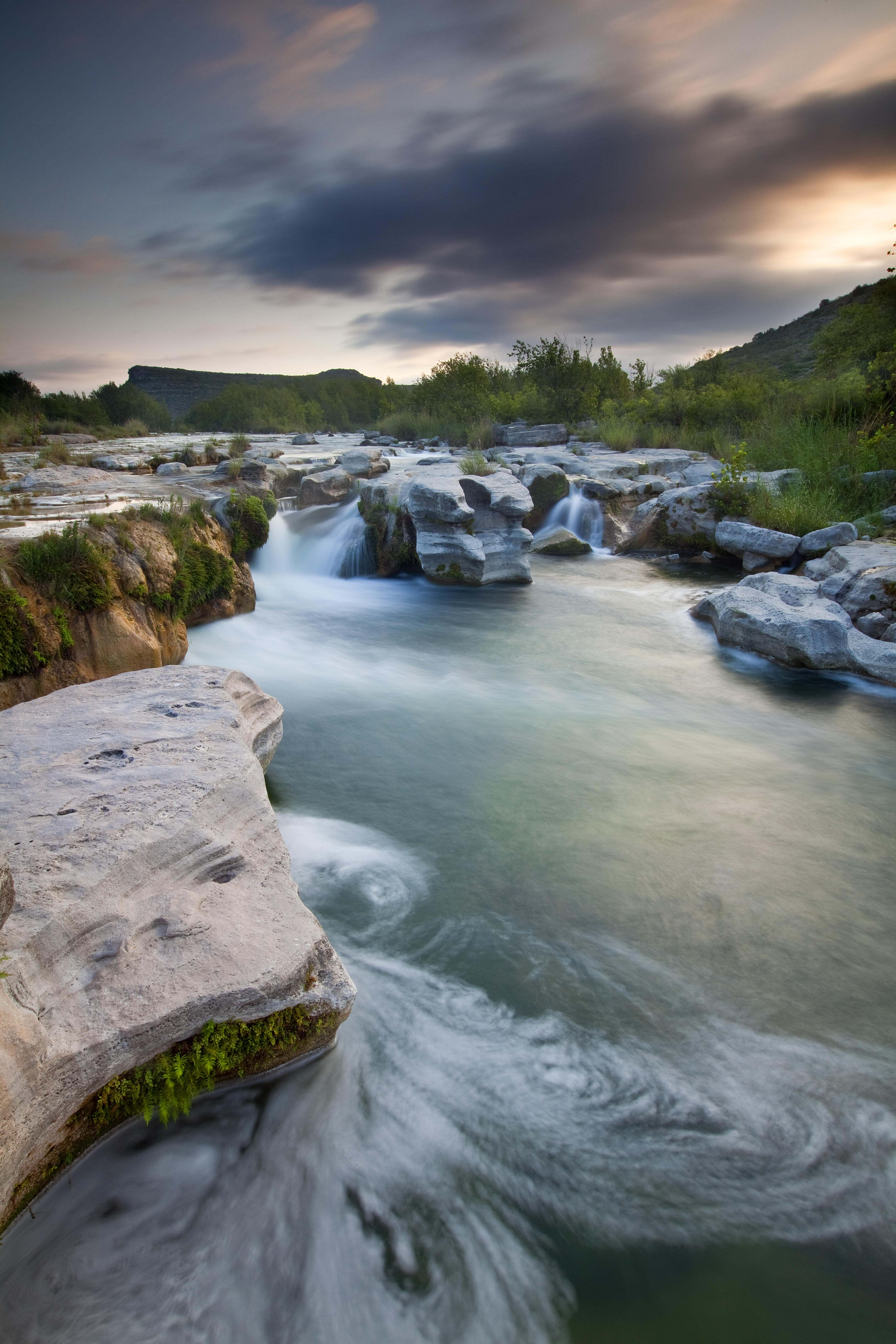 Boulders dot clear blue waters, creating water falls.